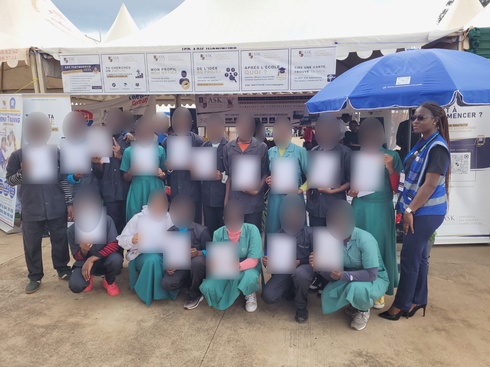 Devant le stand de ASK au CAMBE Ouest 2026, un groupe d’élèves en blouse présente son certificat de participation, aux côtés d’une membre de l’équipe de ASK en gilet ; les noms inscrits sur les certificats sont floutés.