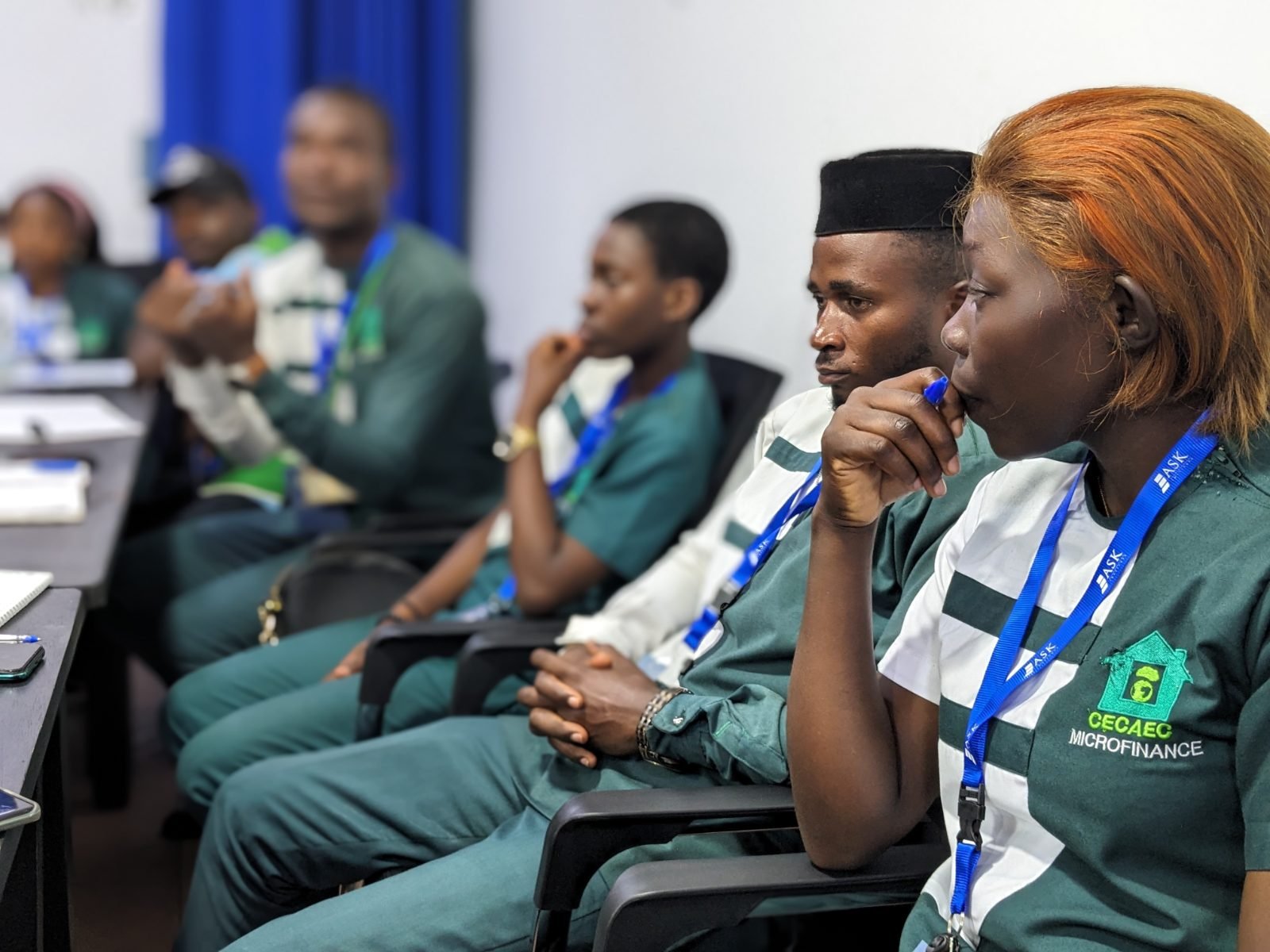 Des participants de la CECAEC COOP-CA, assis en rang, suivent attentivement la présentation ; au premier plan, une participante tient un stylo près de son visage.