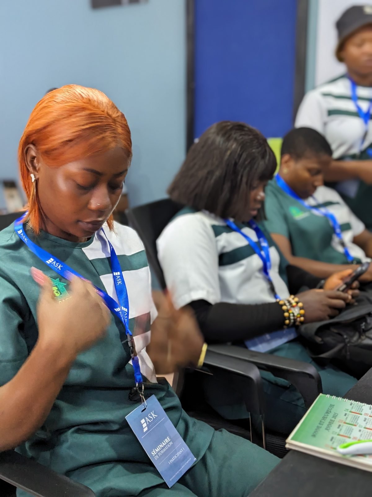 Des participantes, badge « Séminaire de formation, participant » au cou, s’installent dans la salle.