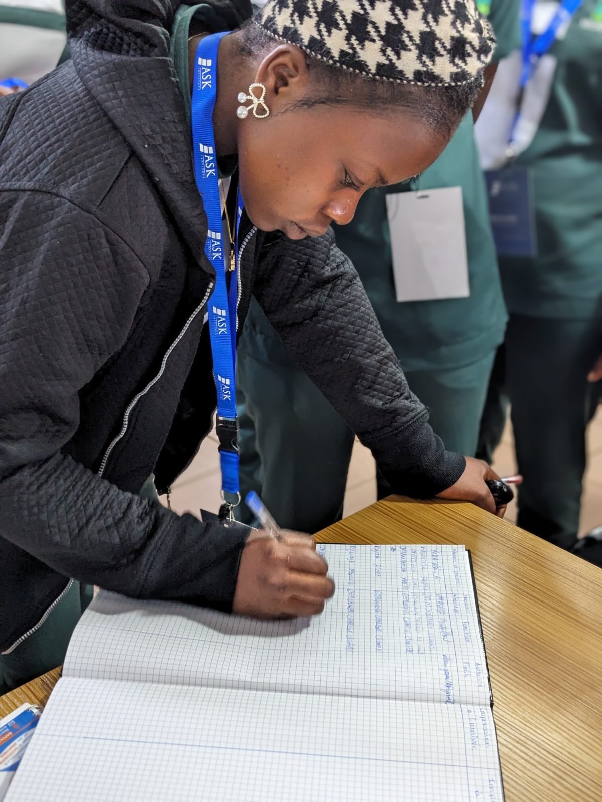 Une participante, badge de ASK Institute au cou, signe le registre de présence posé sur une table.