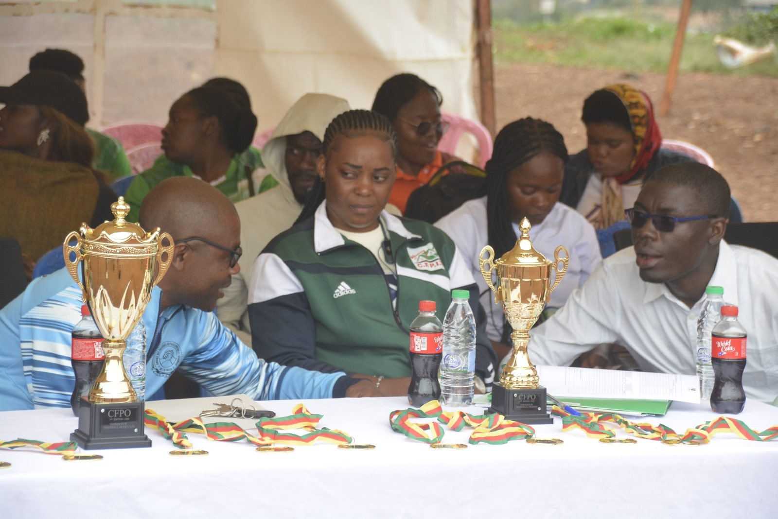 À la table officielle, sous la tente, des personnalités assises derrière les trophées et les médailles alignés.