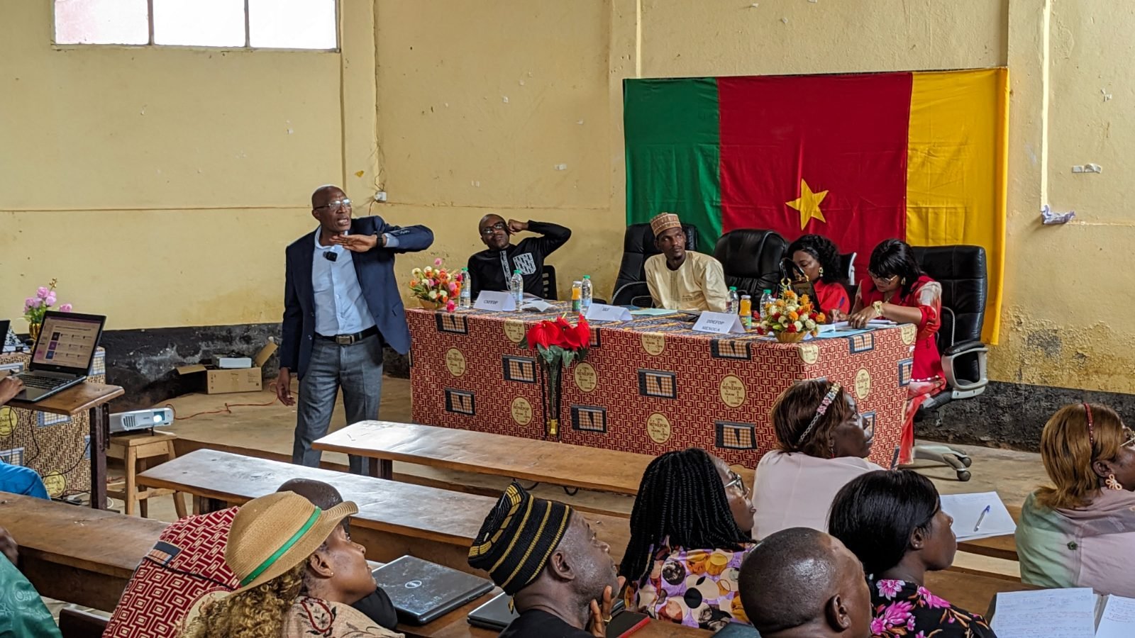 Un intervenant s’adresse aux participants devant la table officielle de la session, où figurent les chevalets du CNFFDP et de la DDEFOP de la Menoua.