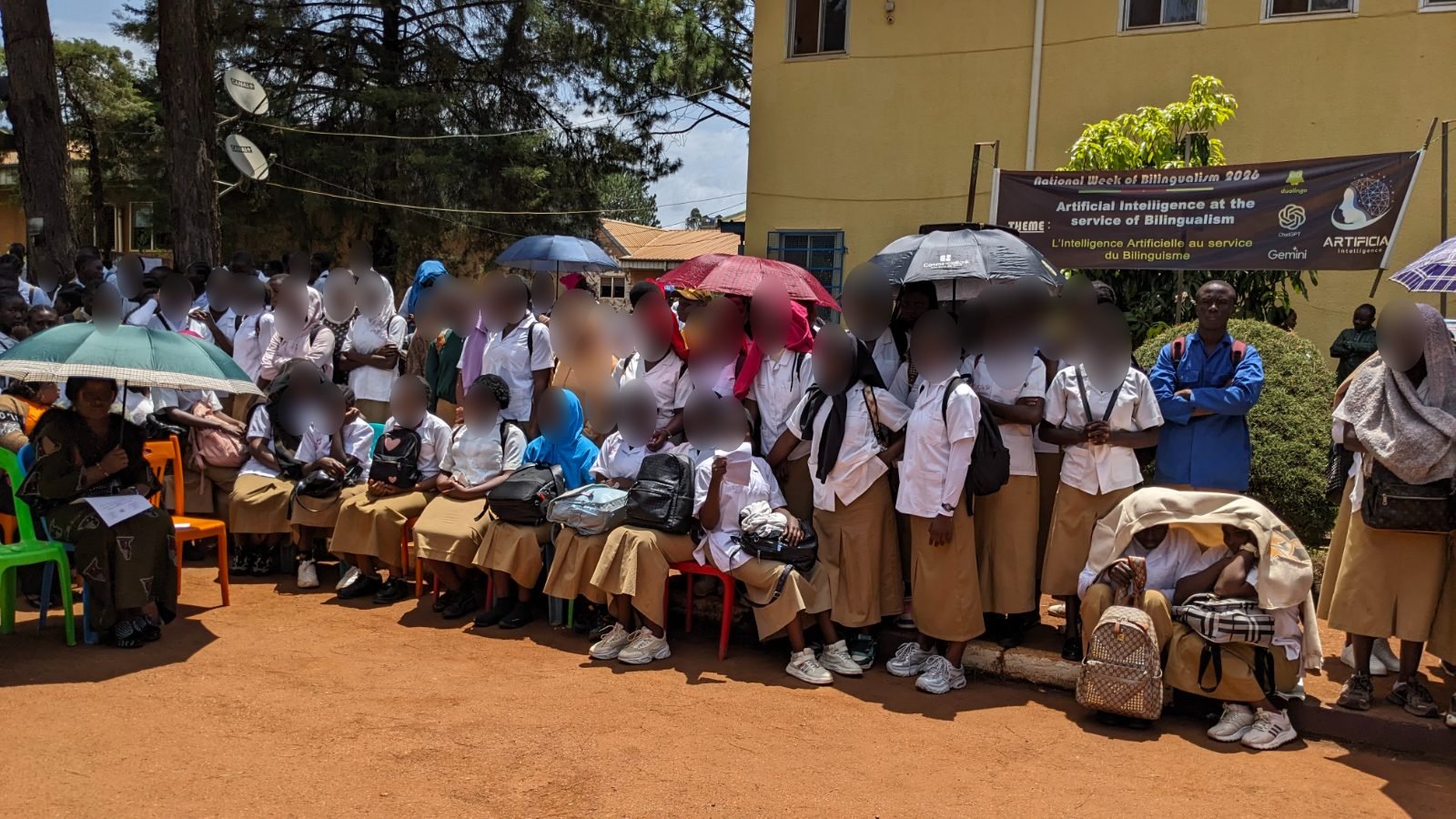 Des élèves en uniforme, assis en rang et debout devant un bâtiment du lycée, suivent la cérémonie.