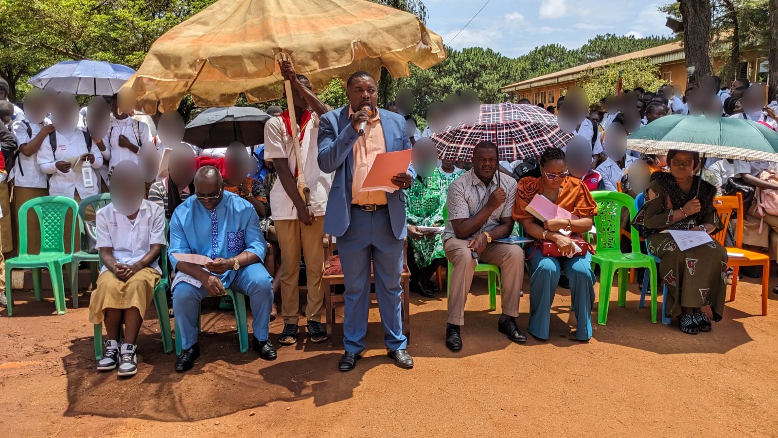 Sous des parasols, un orateur en costume prend la parole au micro devant les autorités assises et les élèves du Lycée Technique de Bafoussam rassemblés derrière elles.