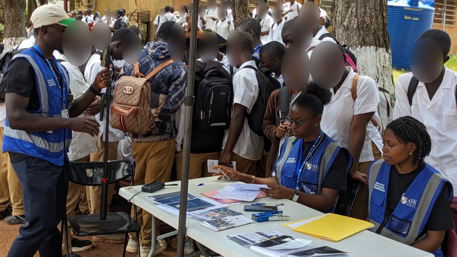À la table du stand couverte de brochures de ASK Institute, deux membres de l’équipe en gilet conseillent les élèves qui se pressent autour d’eux.