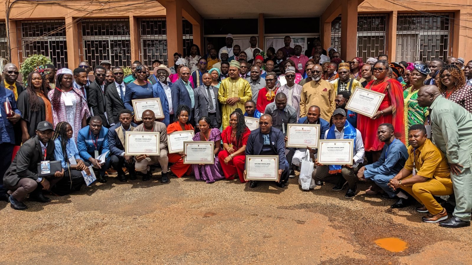 Photo de groupe des participants de la réunion sectorielle devant un bâtiment ; plusieurs d’entre eux présentent un diplôme d’excellence.